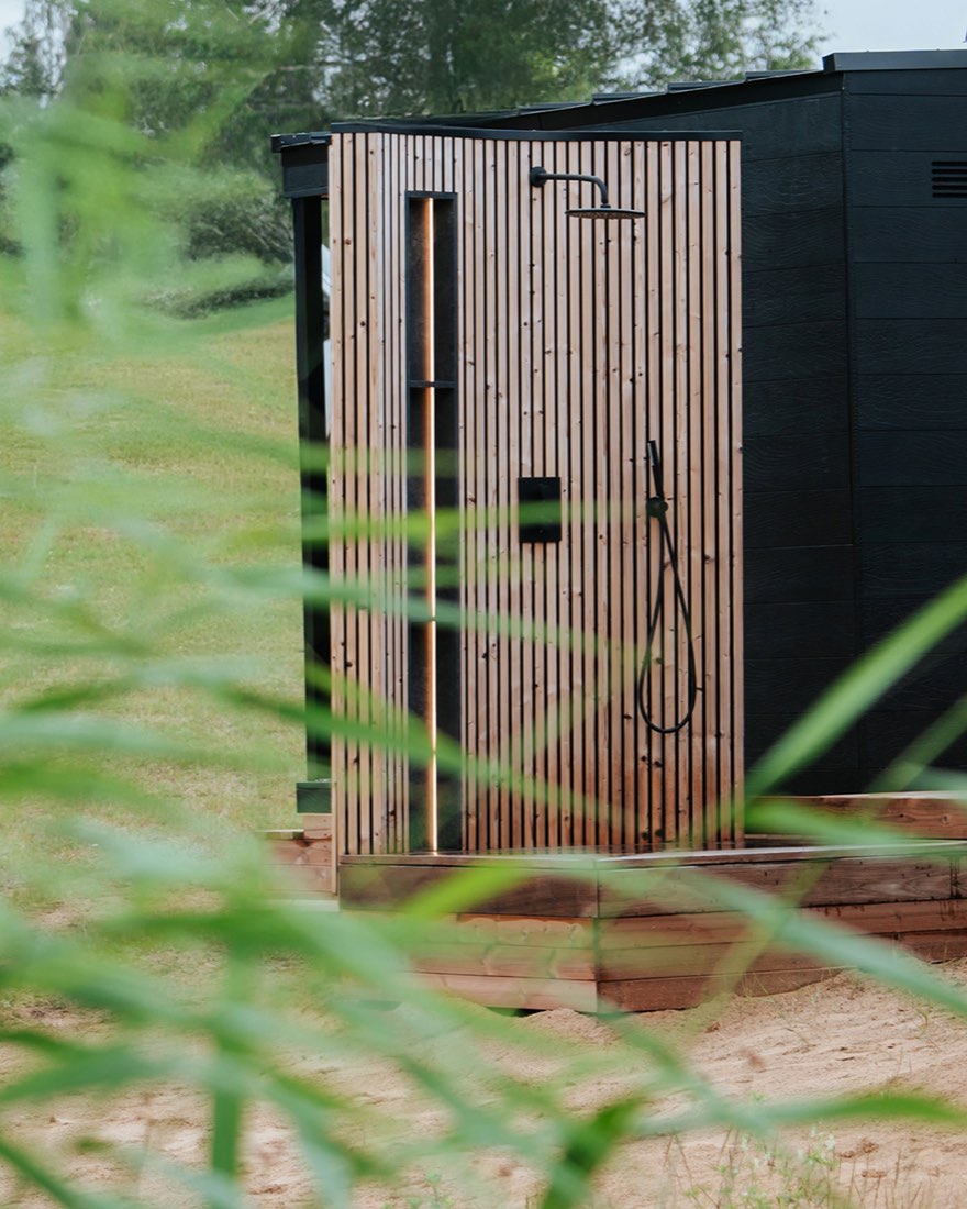 Outdoor shower in slatted wood beside a black sauna cabin